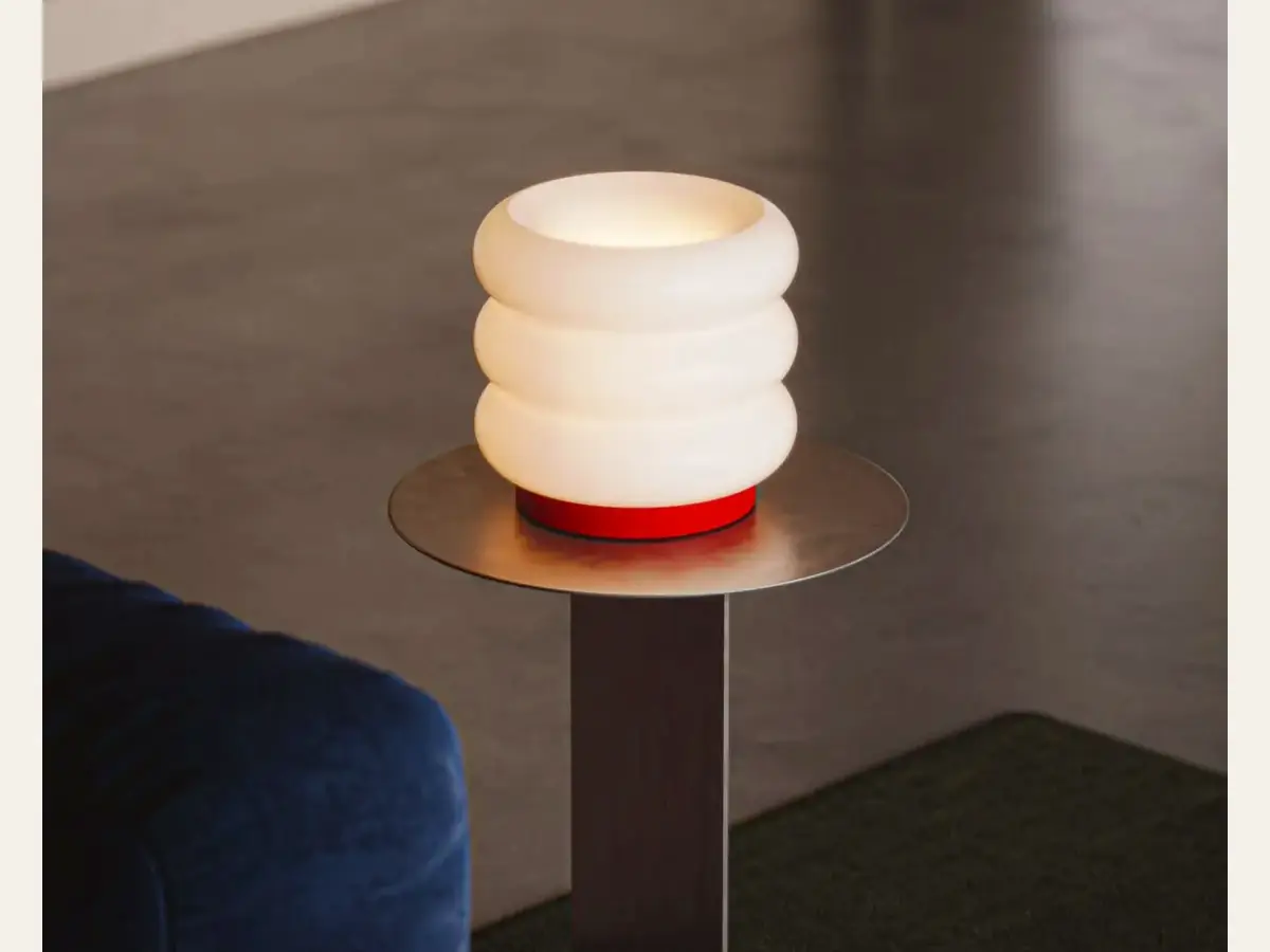 A ribbed glass table lamp glowing on a slim side table.