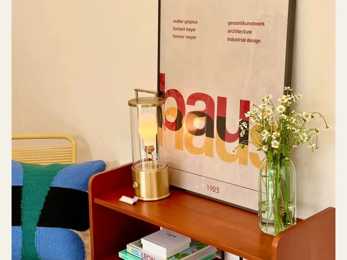 A colourful shelf styled with a rechargeable lamp, flowers, and a poster.
