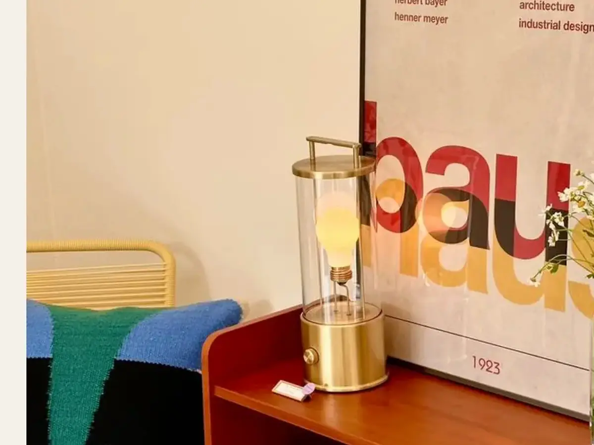 A brass portable lamp beside a framed poster on a red sideboard.